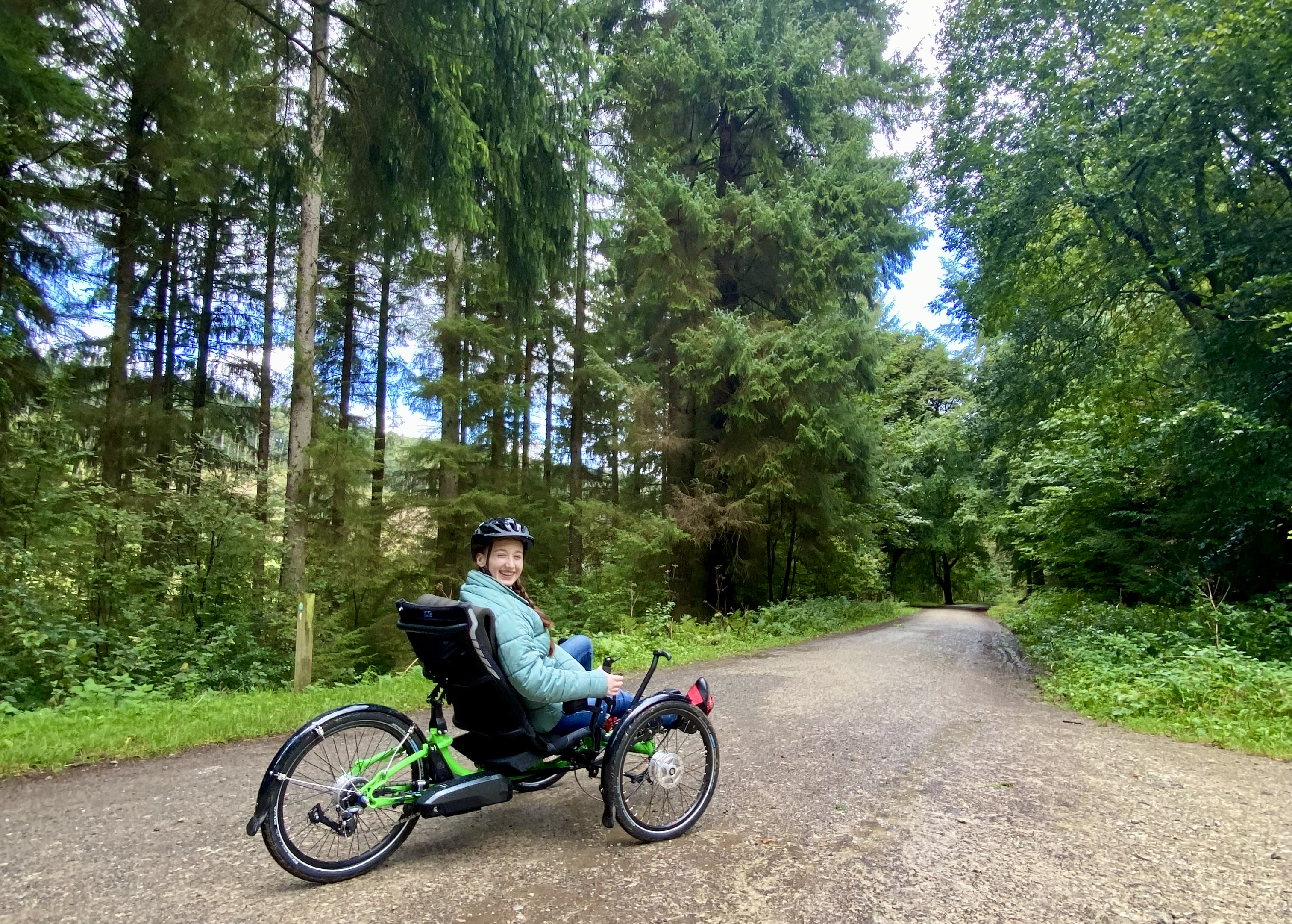 Young woman in a helmet on an accessible bike cycling on a tree-lined path in Dalby Forest