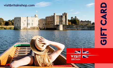 A woman in a summer hat sits in a wooden boat in the moat of Leeds Castle in Kent