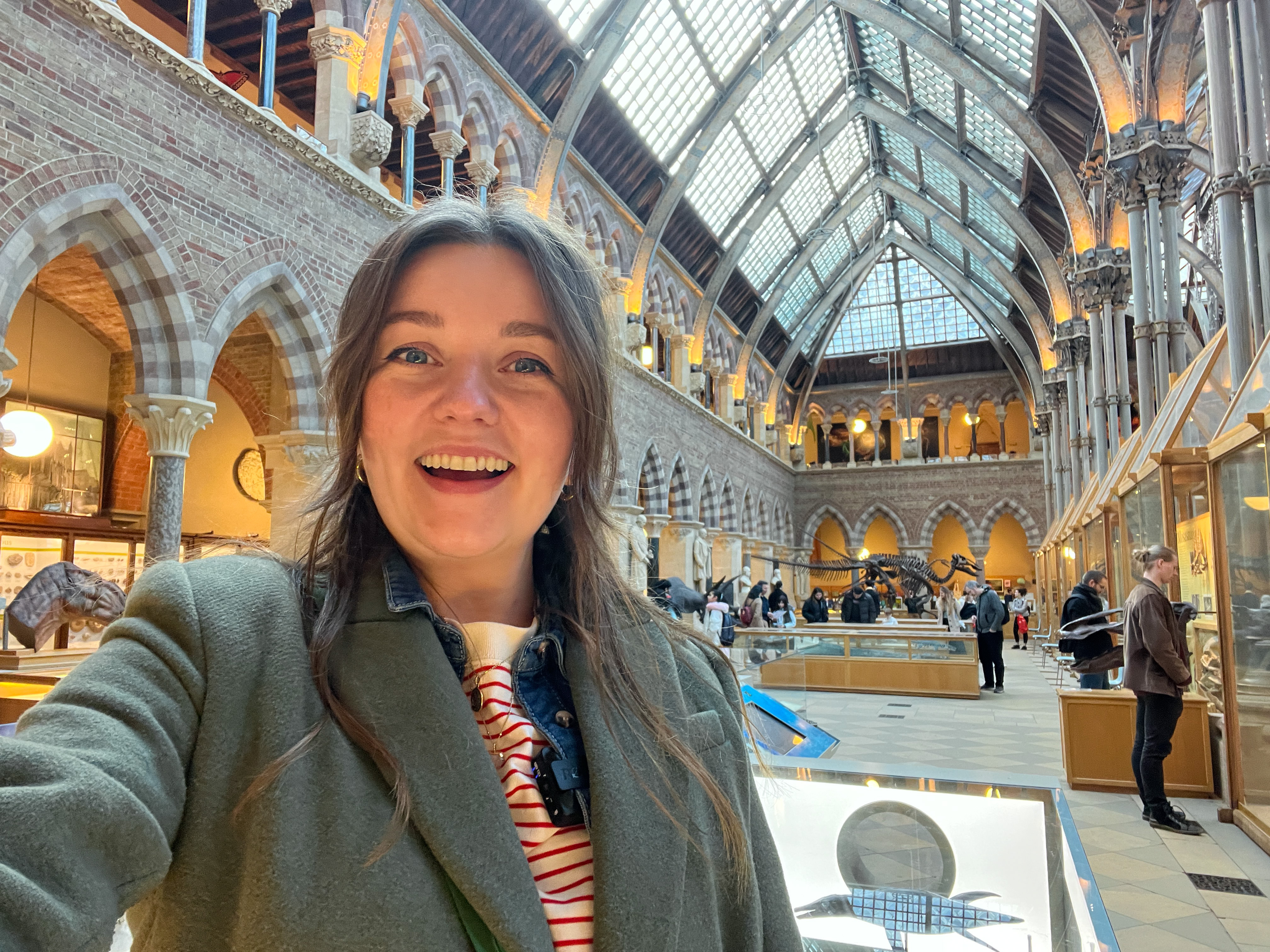 A  smiling woman takes a selfie in the Neo-gothic interior of the University of Oxford Natural History Museum