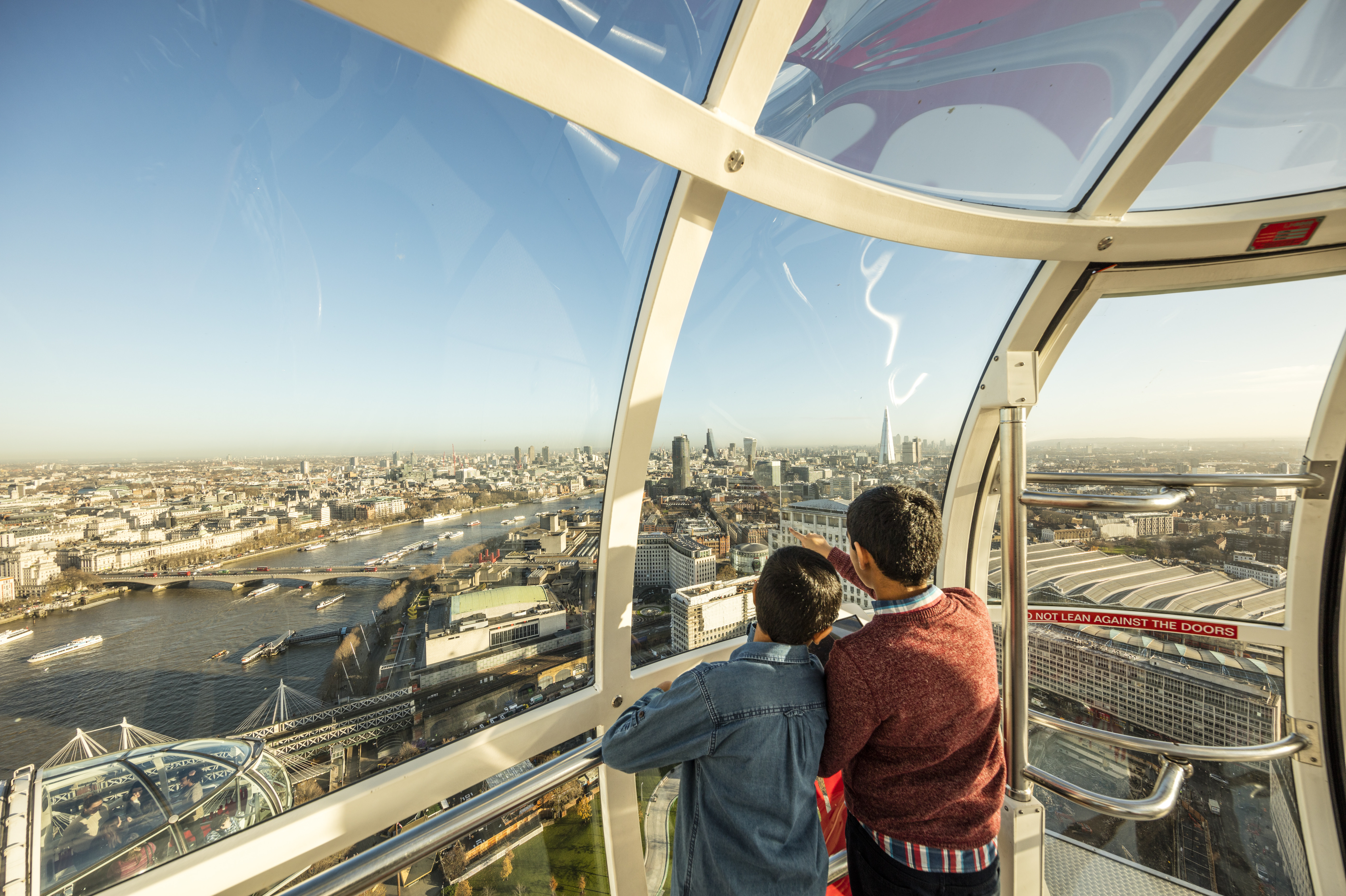 Two boys inside a London Eye glass pod looking at the vast city skyline