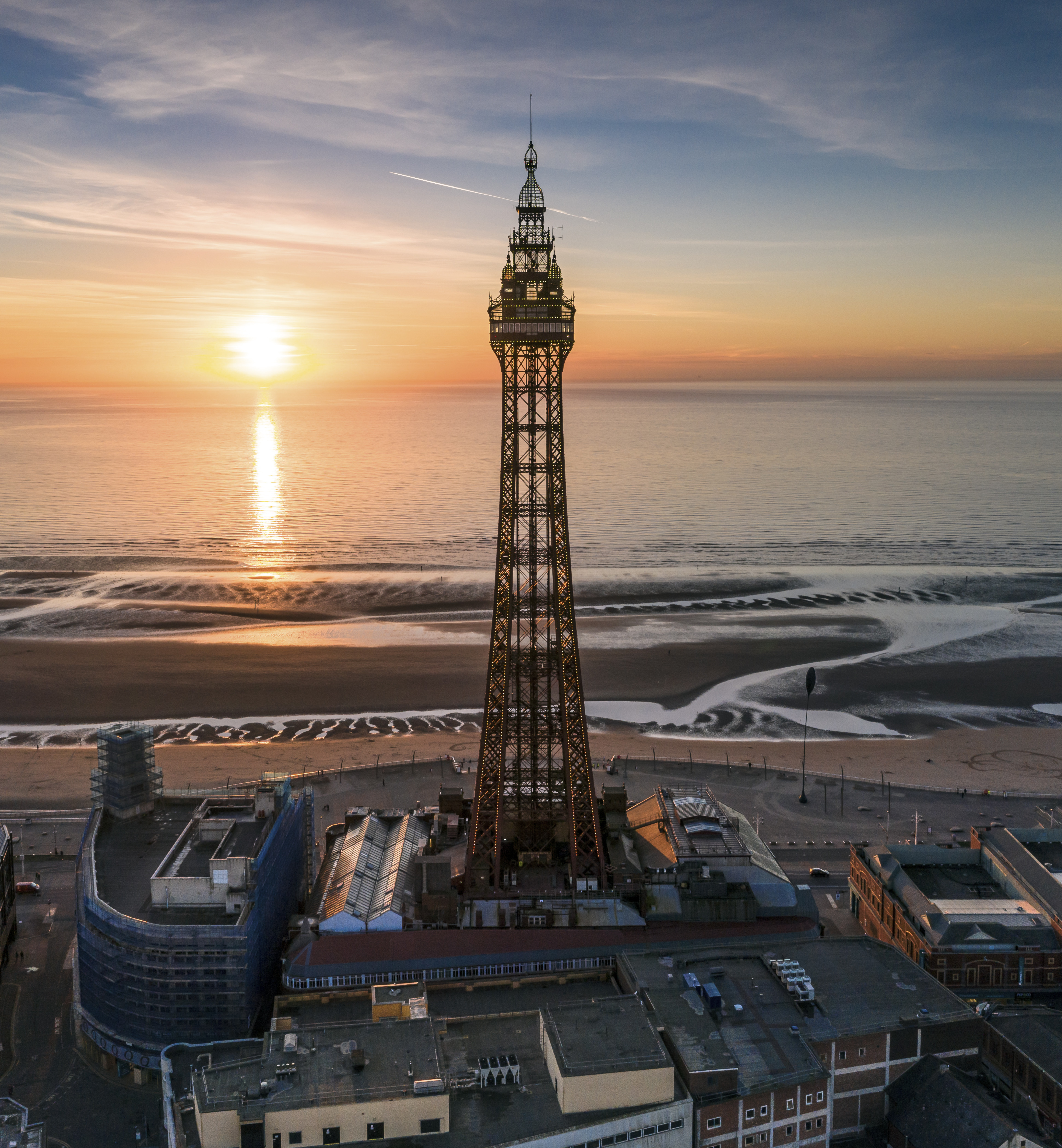 a bird's eye view of Blackpool Tower at sunset, with coast in front of the tower and the town behind it