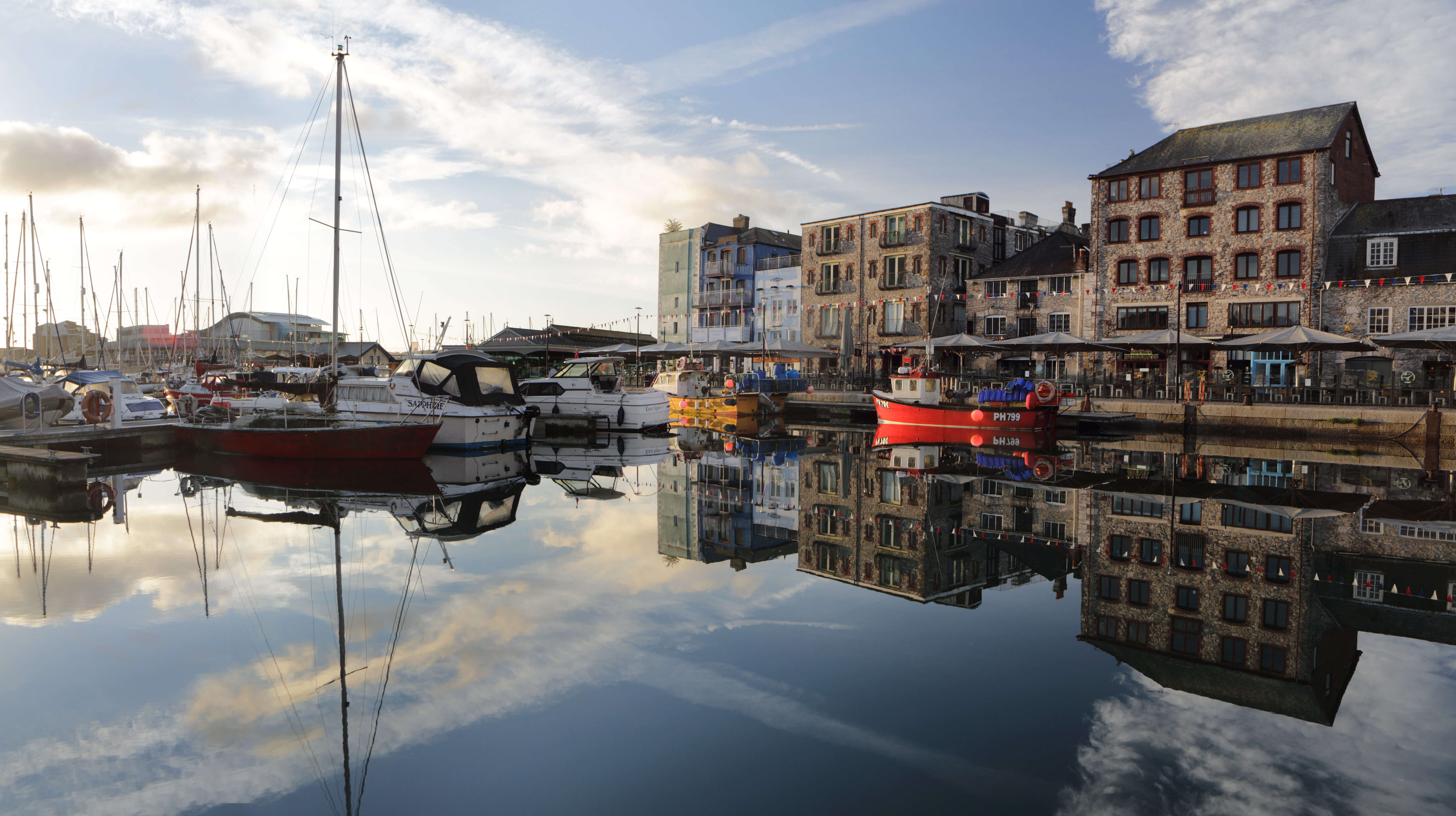 Boats and harbourside buildings reflect in serene water at The Barbican in Plymouth