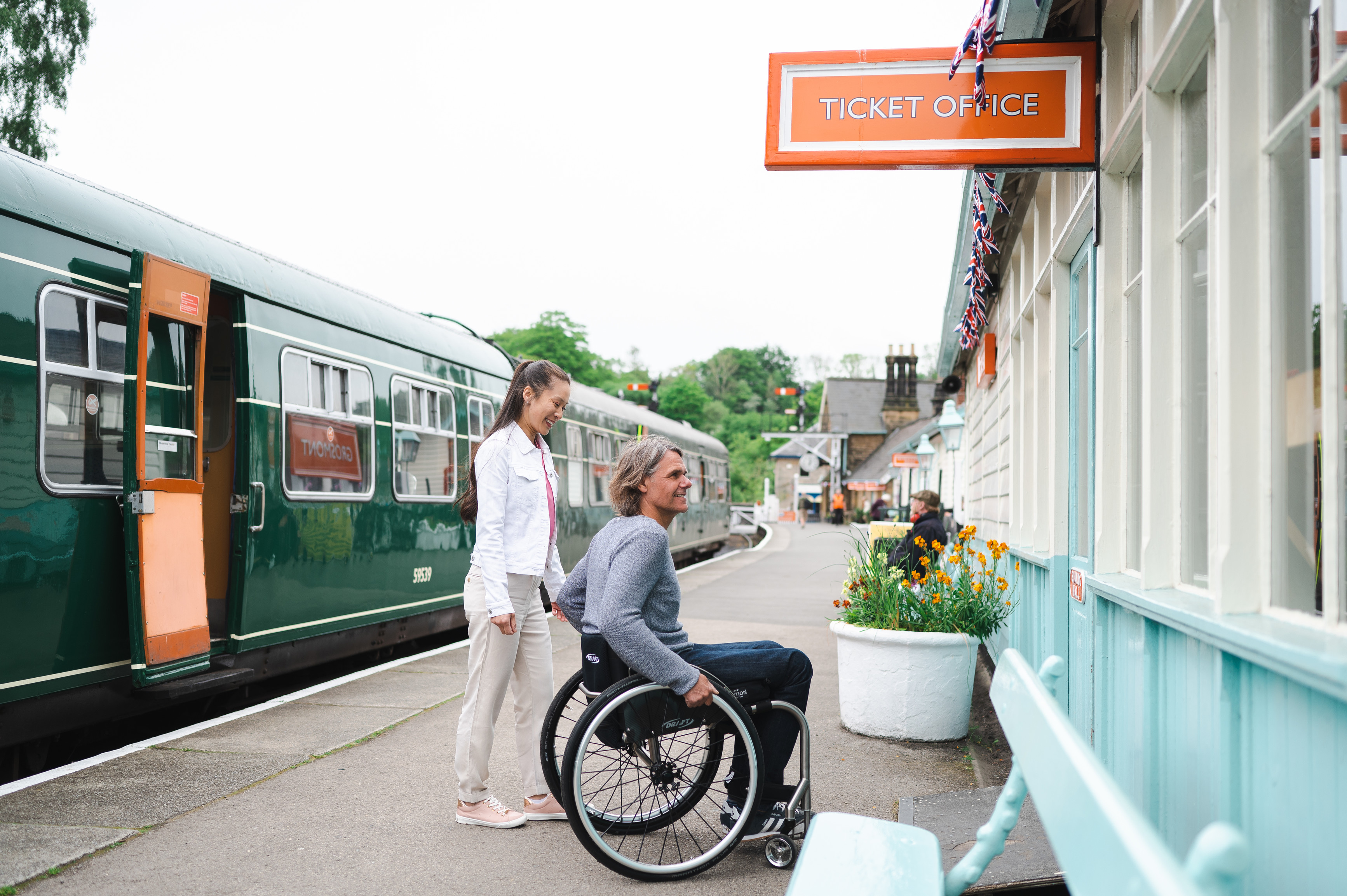 Man using a wheel chair and woman about to go into the ticket office of Grosmont Station