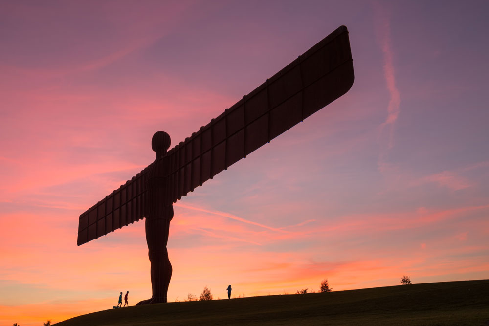 The wings of the Angel of the North stretch across a pink sky