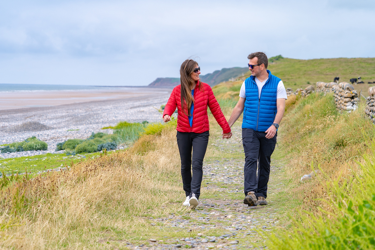 Two people holding hands walking along grassy coast path