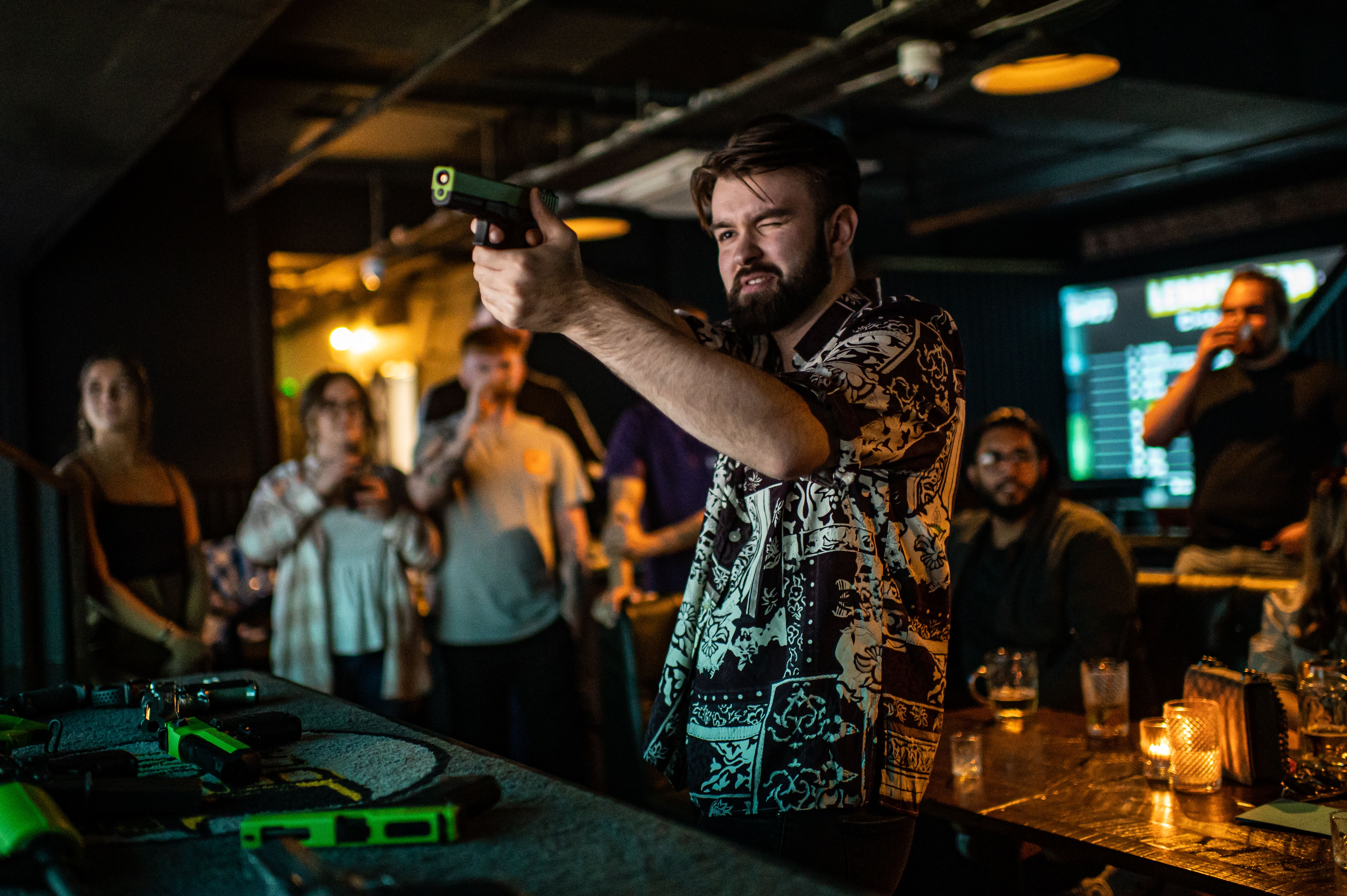 Man aiming replica gun while people drink around him