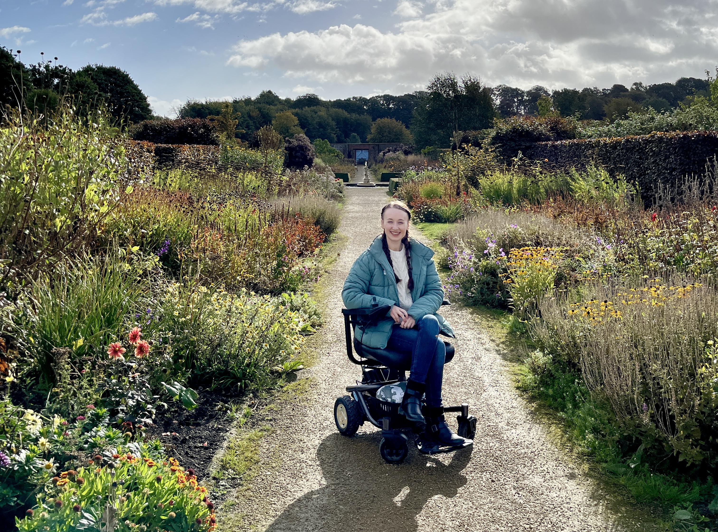 Young woman in a wheelchair on a path surrounded by flowers and bushes at Helmsley Walled Garden