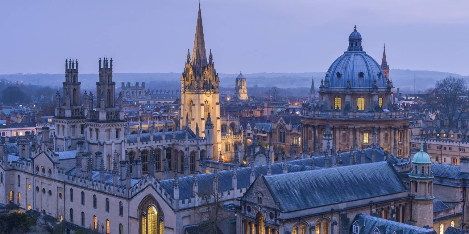 View from a height over the rooftops of Oxford city, the historic buildings and the landmarks of the university city. Night. Buildings lit up.