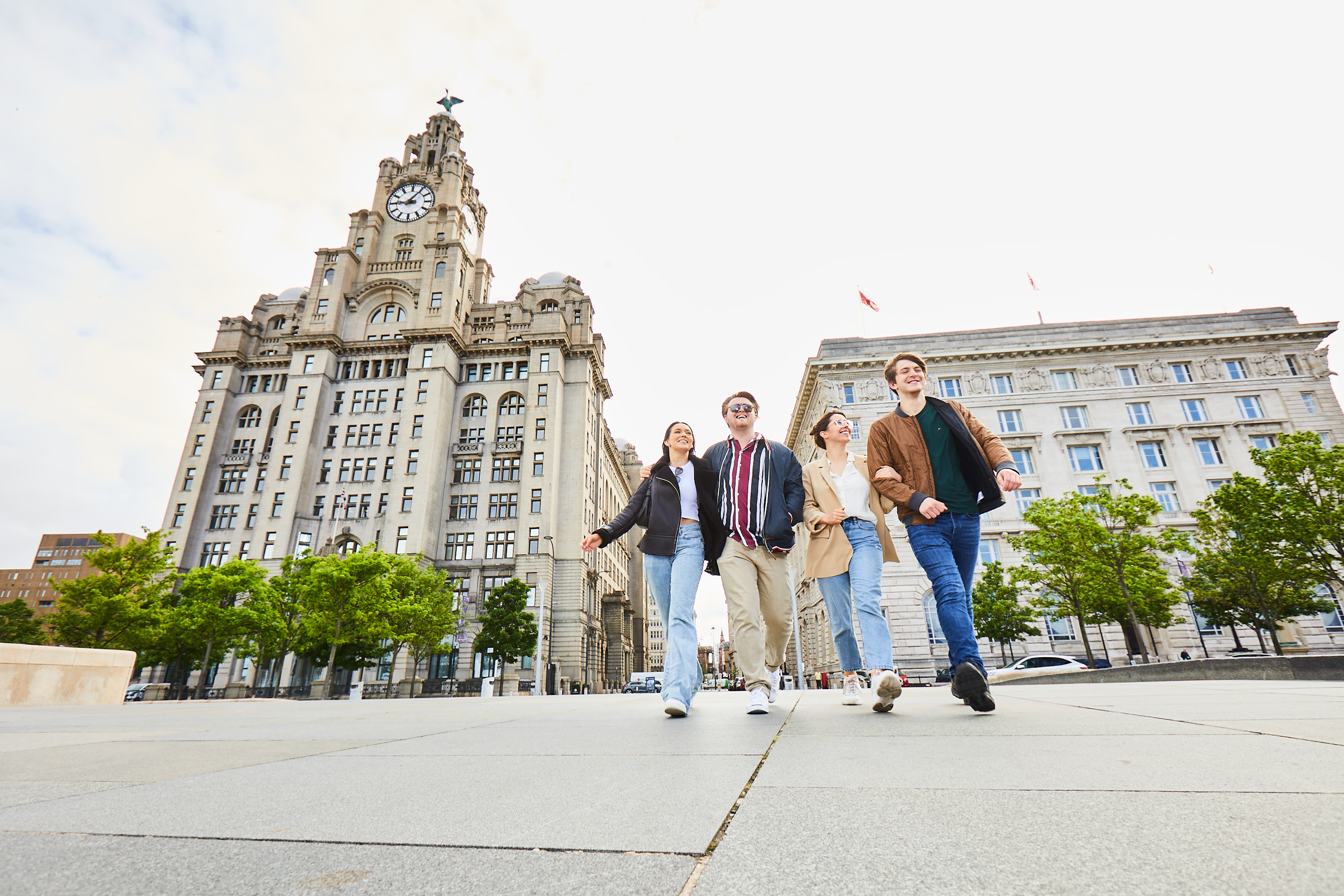 Four smiling friends walking outside the Royal Liver Building