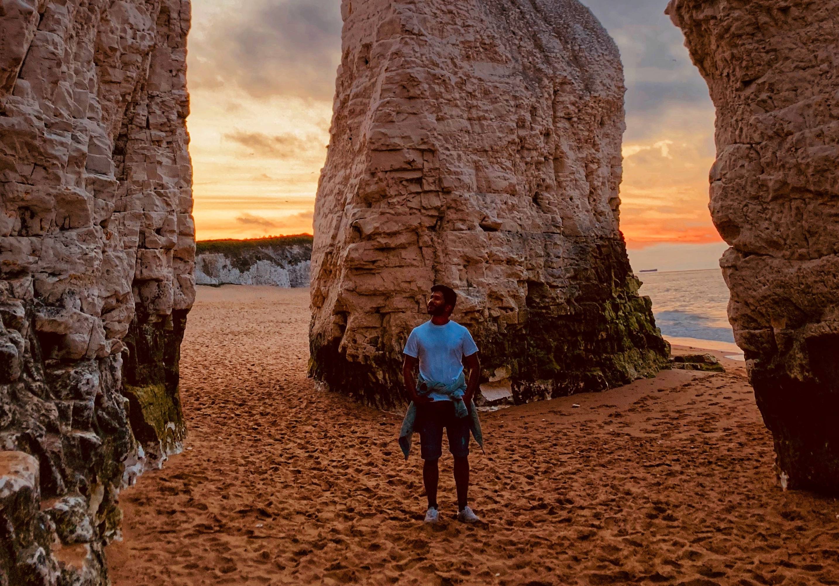 Man stands between two sandstone formations on a beach at sunset