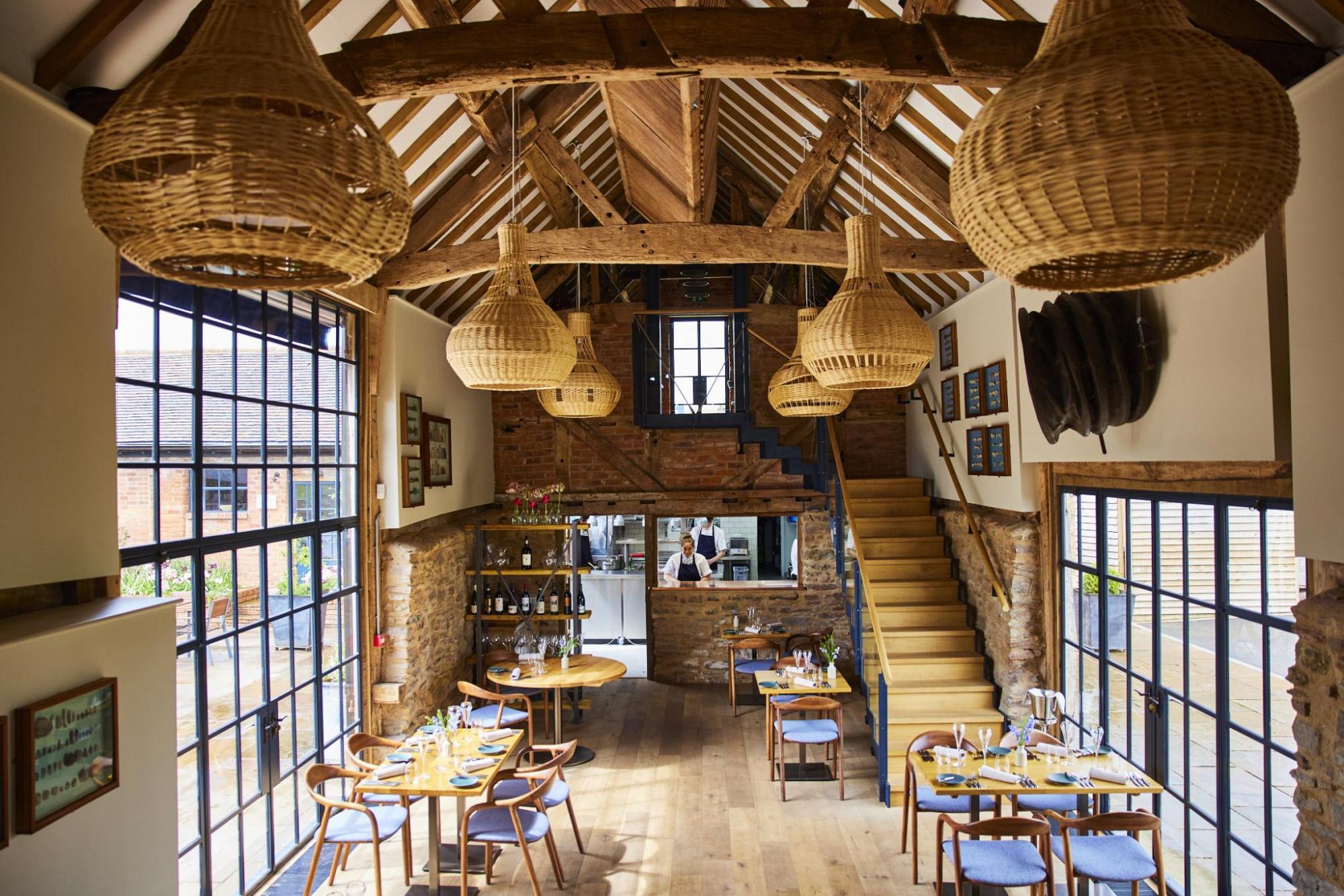 Interior shot of glass-side restaurant with wooden vaulted ceiling and open view of kitchen in rear