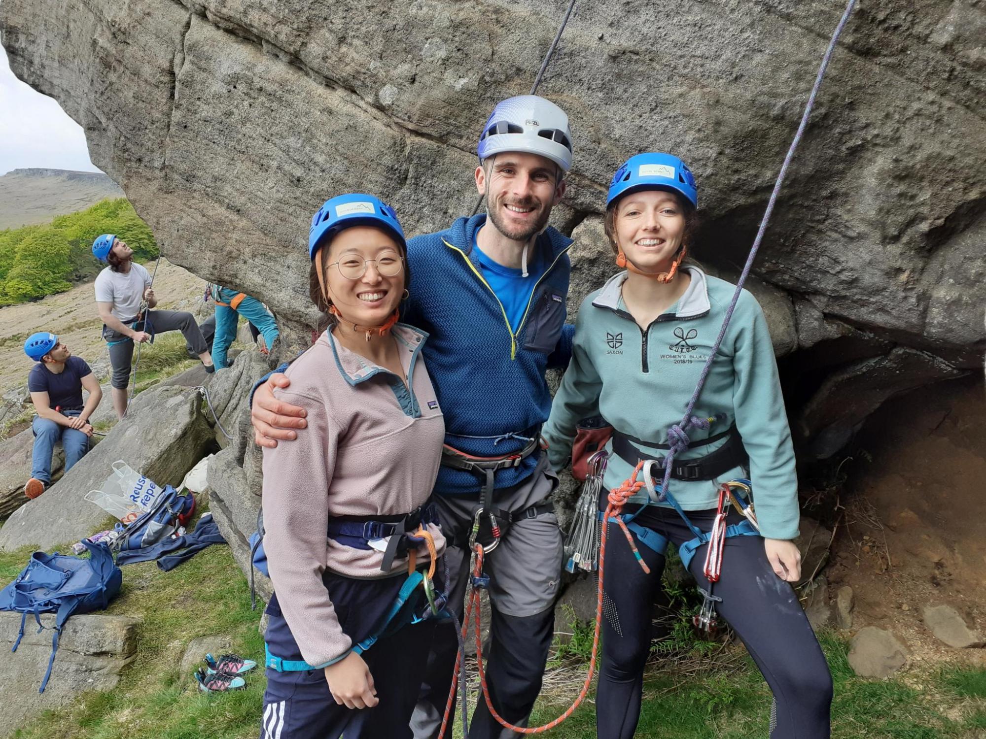 Three rock climbers pose smiling in front of a large boulder