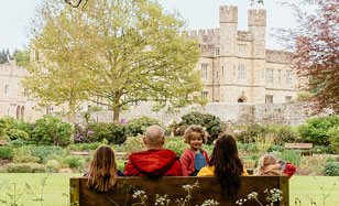 Family sit on a bench infront of Leeds Castle in Kent