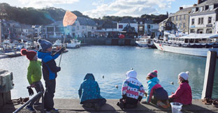 Children on harbour wall fishing for crabs, Padstow Harbour, Padstow, Cornwall, England.