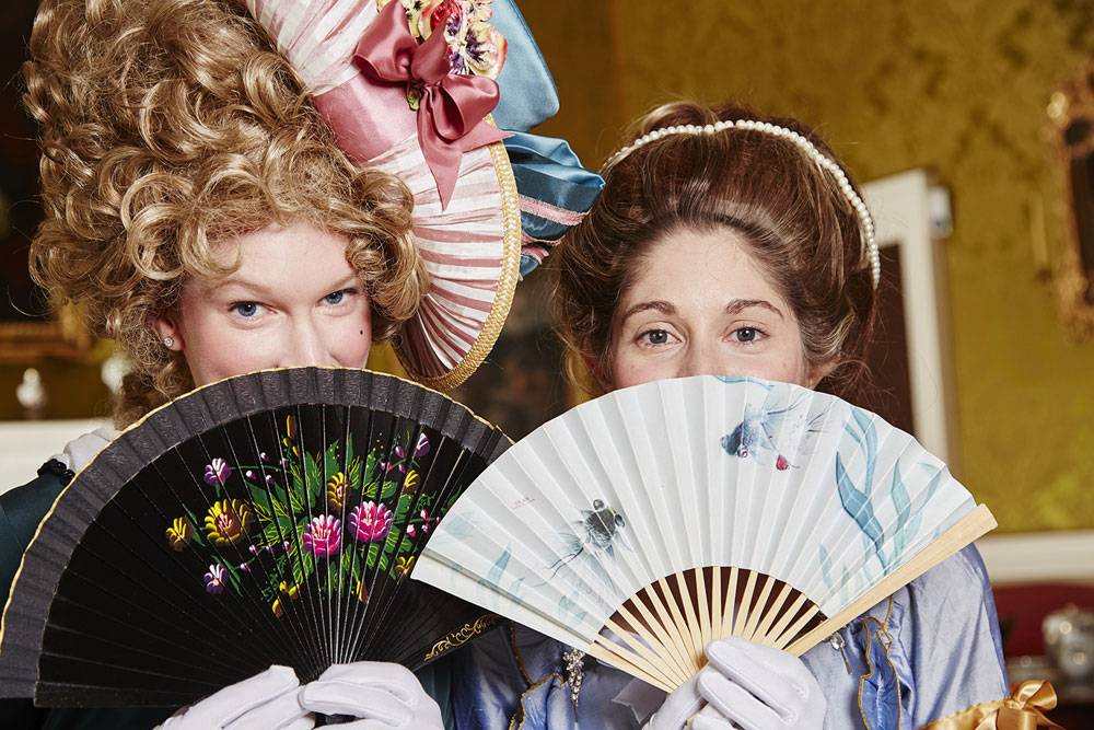 Two ladies in georgian fancy conceal their faces with fans