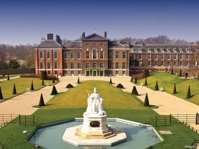 The view from the front of the Kensington Palace, a Baroque royal residence set in Kensington Gardens, in London, with a statue of Queen Victoria in white marble just in the middle of a water fountain in front of the palace's main entrance