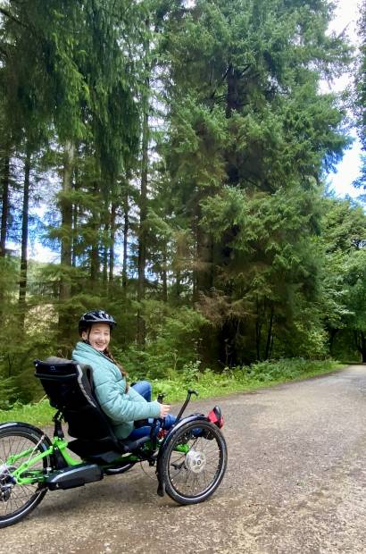 Young woman in a helmet on an accessible bike cycling on a tree-lined path in Dalby Forest