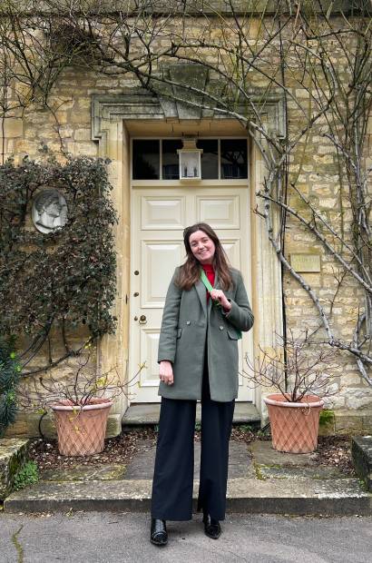 Cheap Holiday Expert blogger Chelsea stands outside a typical Cotswolds house that has a cream door, plant pots and famous Cotswolds stone bricks