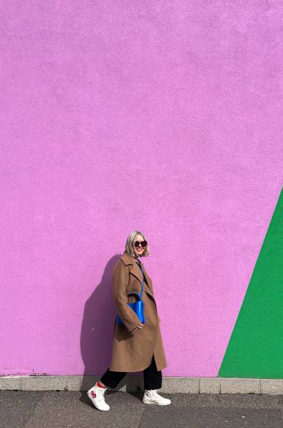 A woman walks past a brightly coloured yellow, pink and green wall 