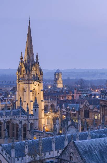 View from a height over the rooftops of Oxford city, the historic buildings and the landmarks of the university city. Night. Buildings lit up.