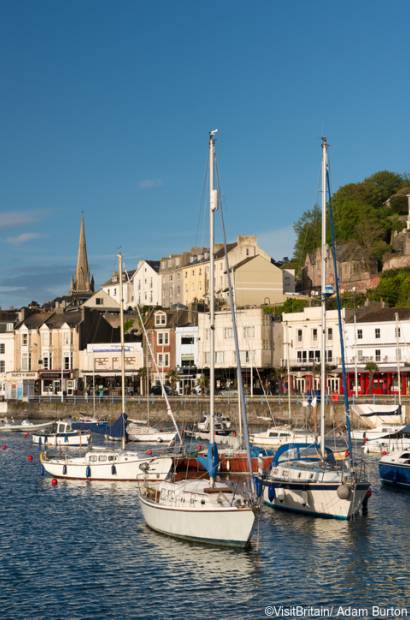 Torquay harbour, a protected mooring for fishing boats, motorboats and sailing boats. Yachts and working boats at anchor. Houses and waterfront buildings.
