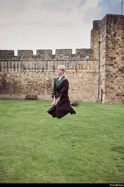 A man in Harry Potter dress riding a broomstick at Alnwick Castle.