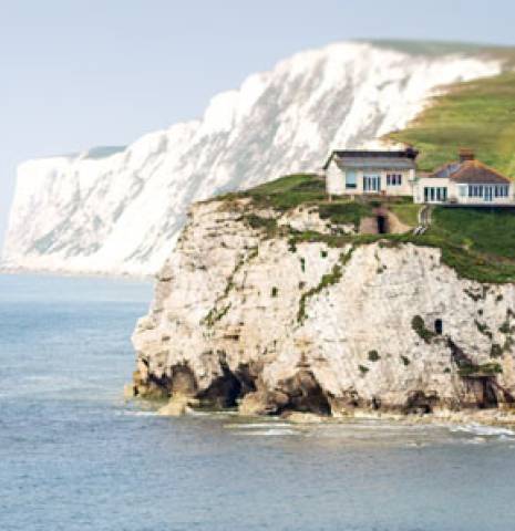 Chalk cliffs topped with grass and white houses and flanked by light blue sea in the Isle of Wight