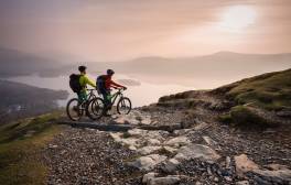 Two people on mountain bikes at the top of a fell at sunset in Borrowdale, Cumbria on the C2C route