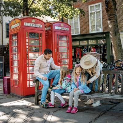 A family sit on a bench in front of two red telephone boxes