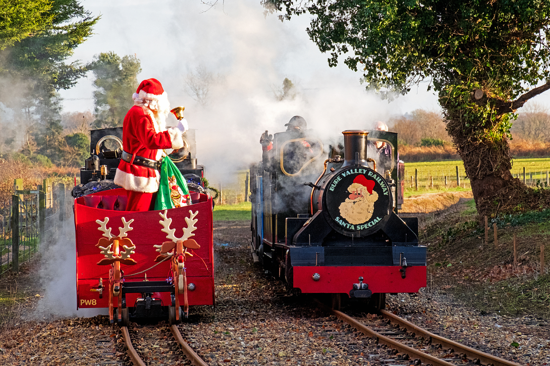 Santa greets the driver of a mini locomotive, in a festive red carriage