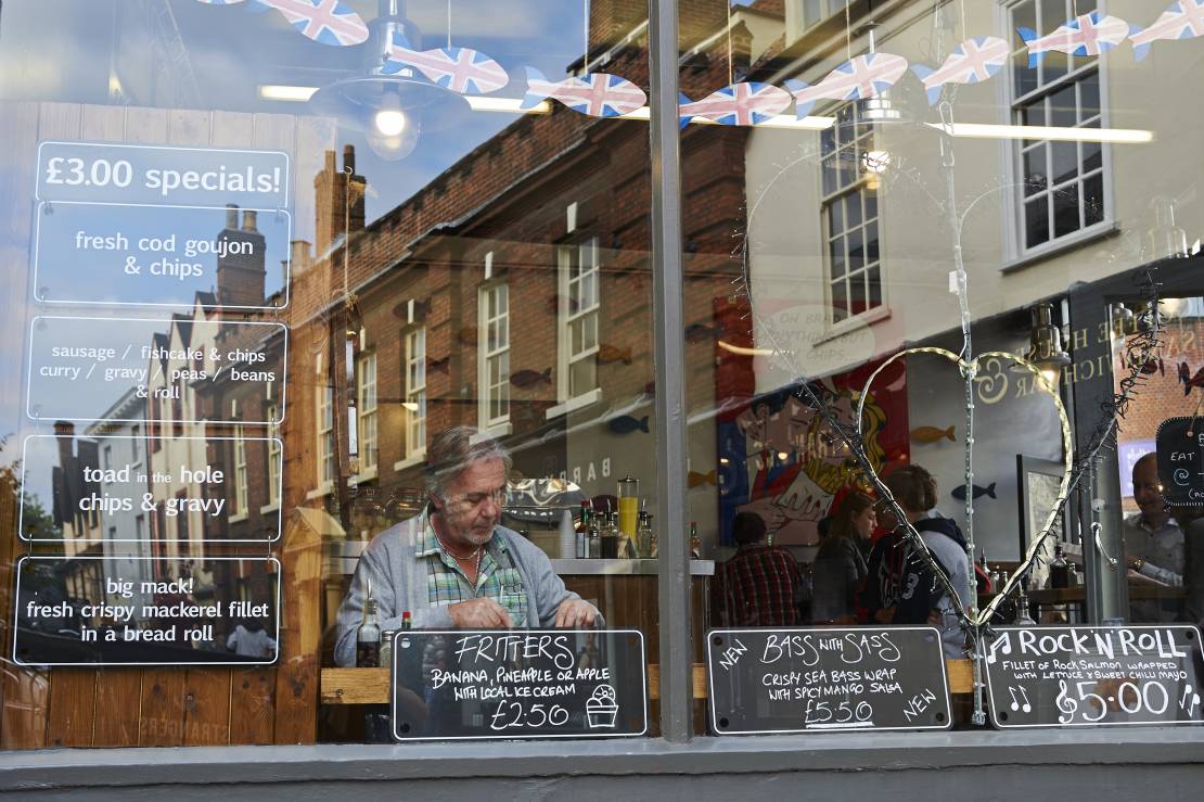 Woman sitting inside Grosvenor Fish Bar, reflection of street in window
