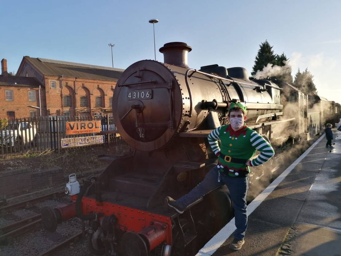 Elf in facemask standing at front of steam train