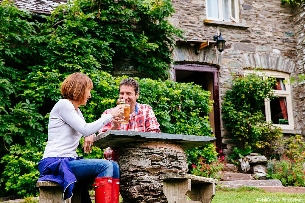 A couple, a man and woman sitting at a table outside a pub, having drinks and a meal. The Tarr Farm Inn near Tarr Steps on the River Barle in Exmoor national park