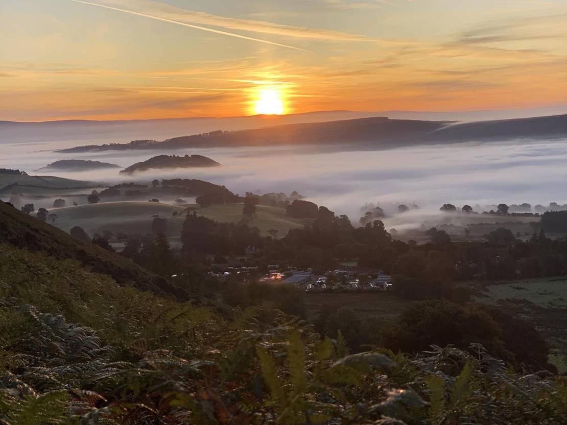 Sunrise over a misty landscape, with a glamping site in the mid distance valley