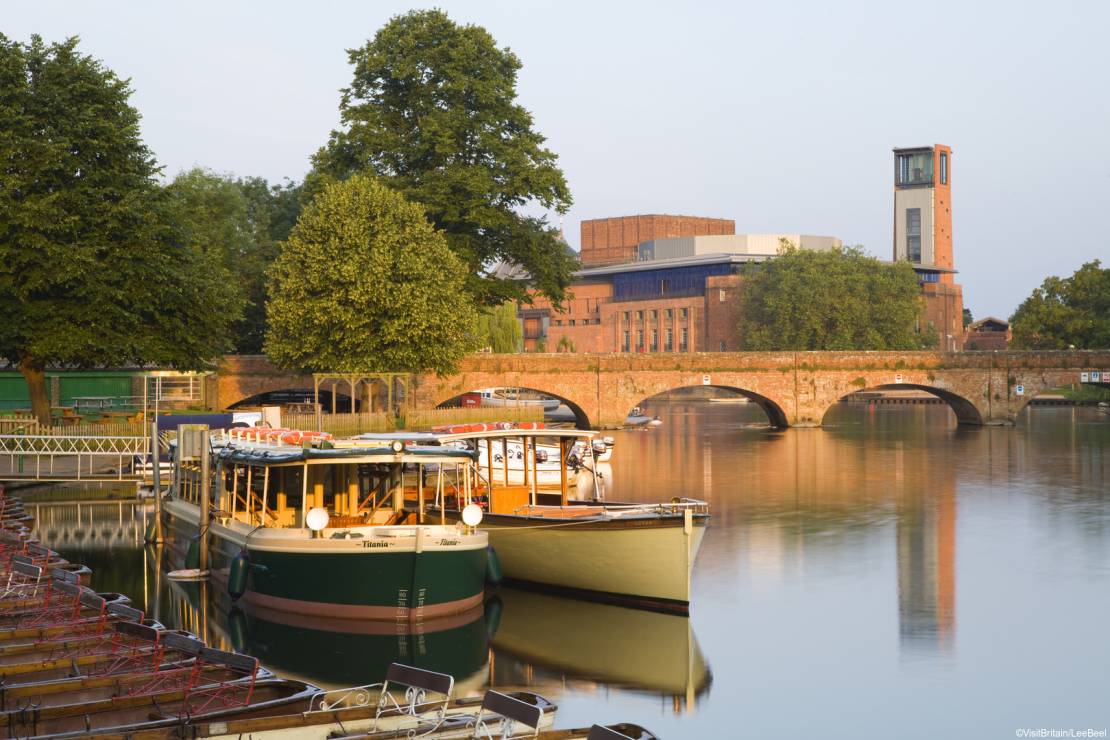 The Royal Shakespeare Theatre. View of the Theatre from the River Avon. Barges and rowboats, passenger boats moored on the river. Bridge across the water