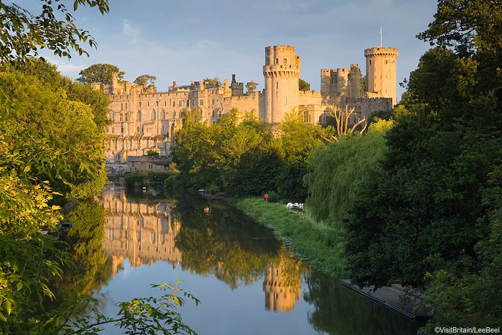 View of Warwick Castle from the River Avon. Grand castle. Trees and green space next to the river.