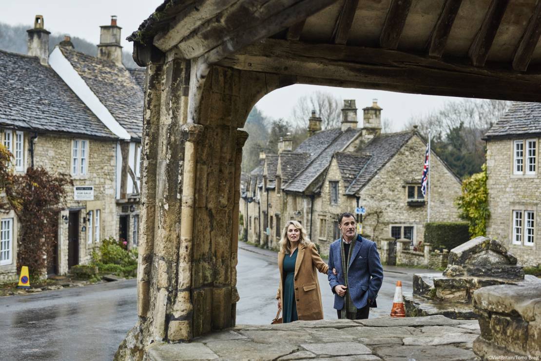 A couple, man and woman, walking arm in arm in the historic village of Castle Combe.