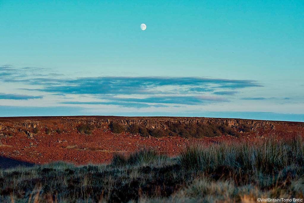 The Peak District National Park. The moon in the early evening sky over the moors of Upper Burbage.