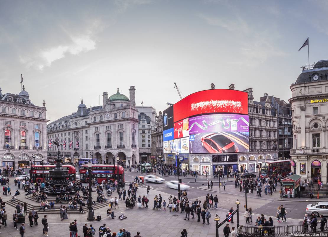  London landmark, Piccadilly Circus and the statue of Eros, and crowds in the centre of London. Buses and cars on the road.
