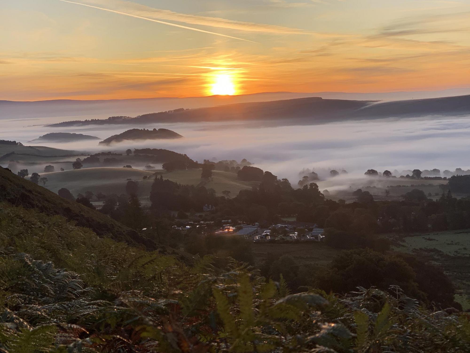 Sunrise over a misty landscape, with a glamping site in the mid distance valley