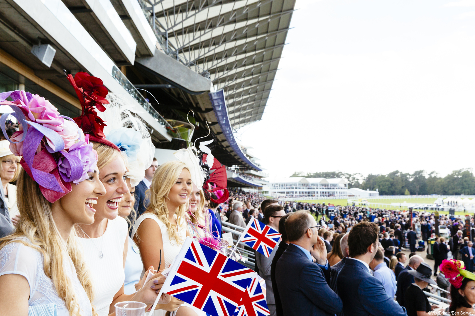 Royal Ascot Race Meeting at the prestigious Ascot racecourse in Berkshire. Smiling young women wearing dresses and hats, watching a race from the grandstand.