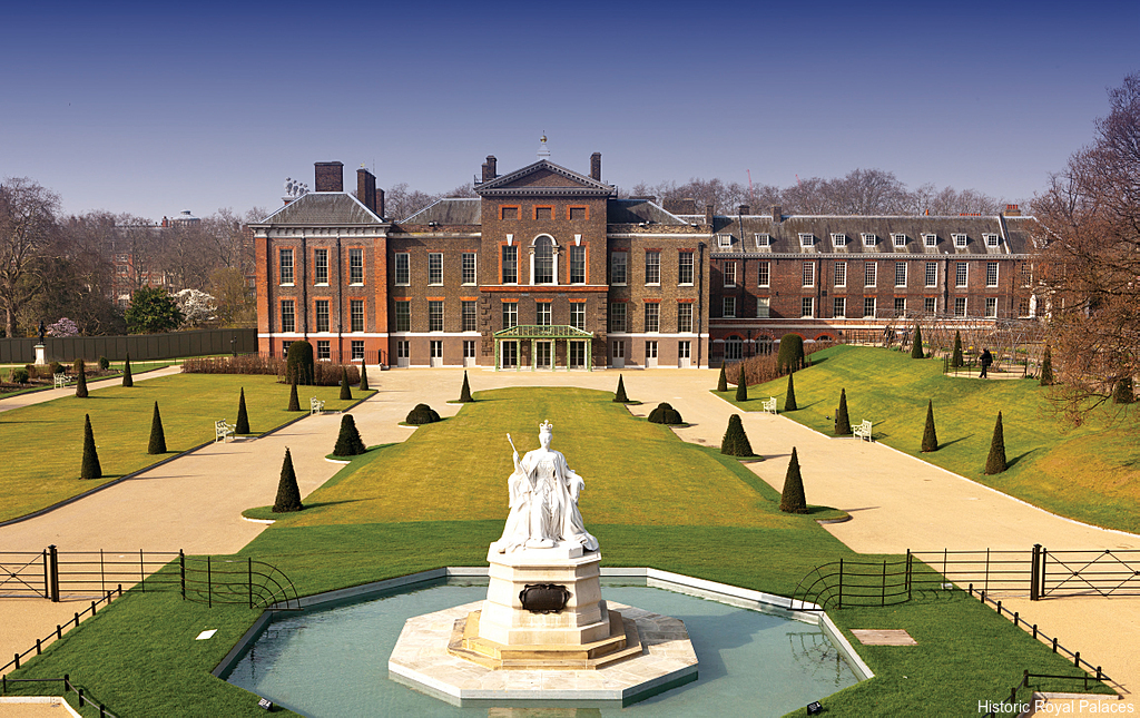 The view from the front of the Kensington Palace, a Baroque royal residence set in Kensington Gardens, in London, with a statue of Queen Victoria in white marble just in the middle of a water fountain in front of the palace's main entrance
