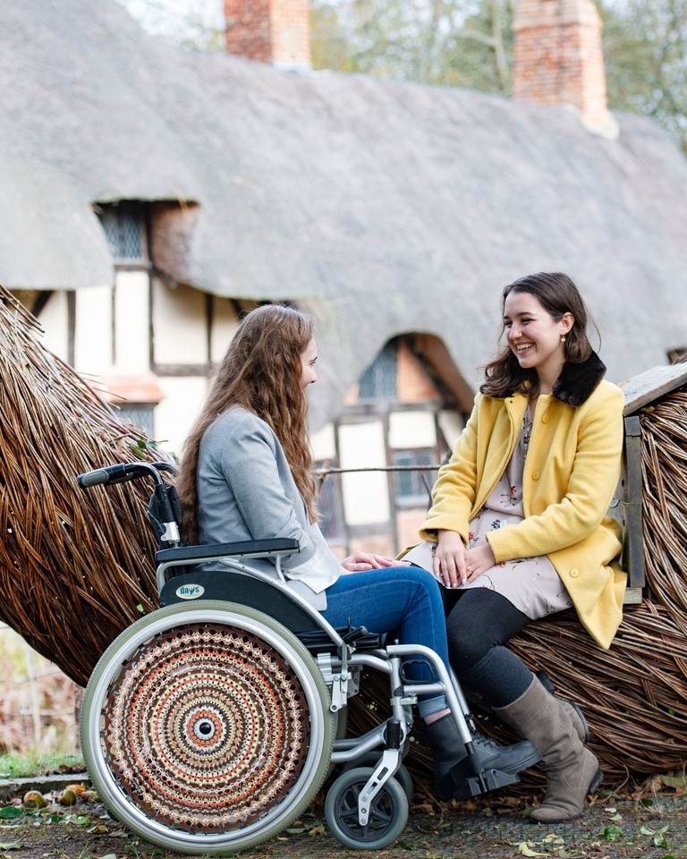 Wheelchair user and friend sat beside a wooden sculpture
