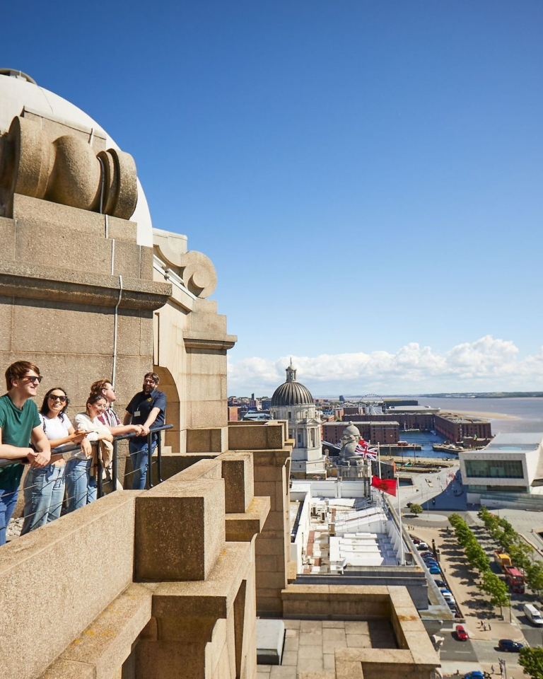A group of visitors standing on a terrace overlooking cityscape by the water