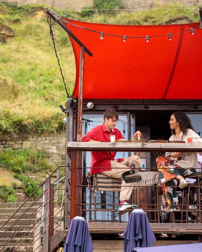 Friends enjoying food and drink at a beachside outdoor cafe.