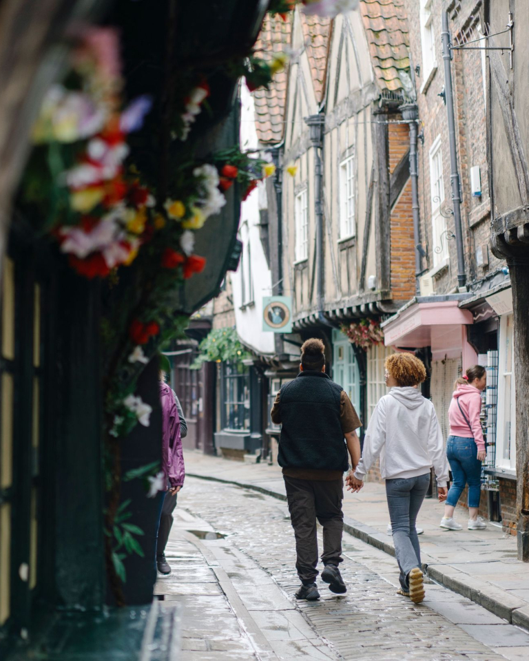 A man and a woman walk down a cobbled street holding hands