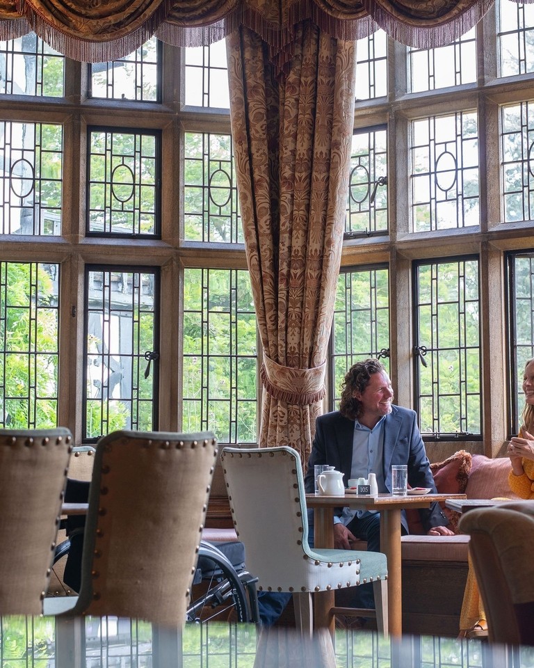 A man and a woman have coffee in a hotel lounge with large windows.