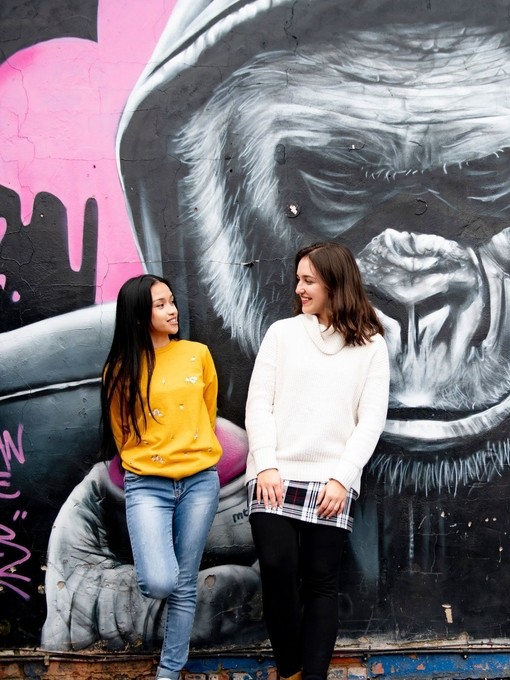 Two women standing in front of painted mural on street wall