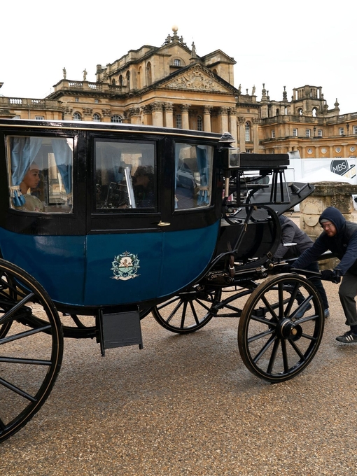 A movie set in a palace grounds with actors in a horse and carriage with film crew.
