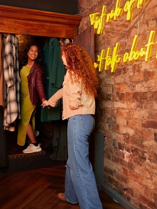 Two women entering a trendy bar through a cupboard.